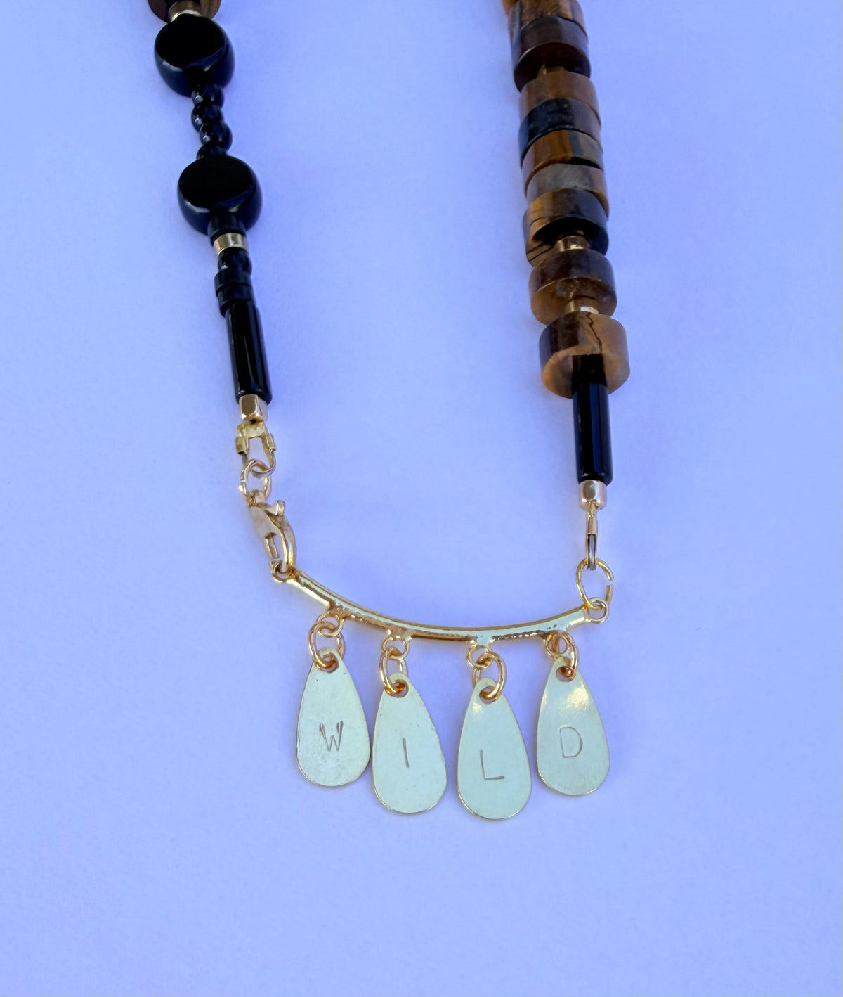 WILD word necklace detail — tuxedo agate and black onyx beads with gold-plated stamped letter charms